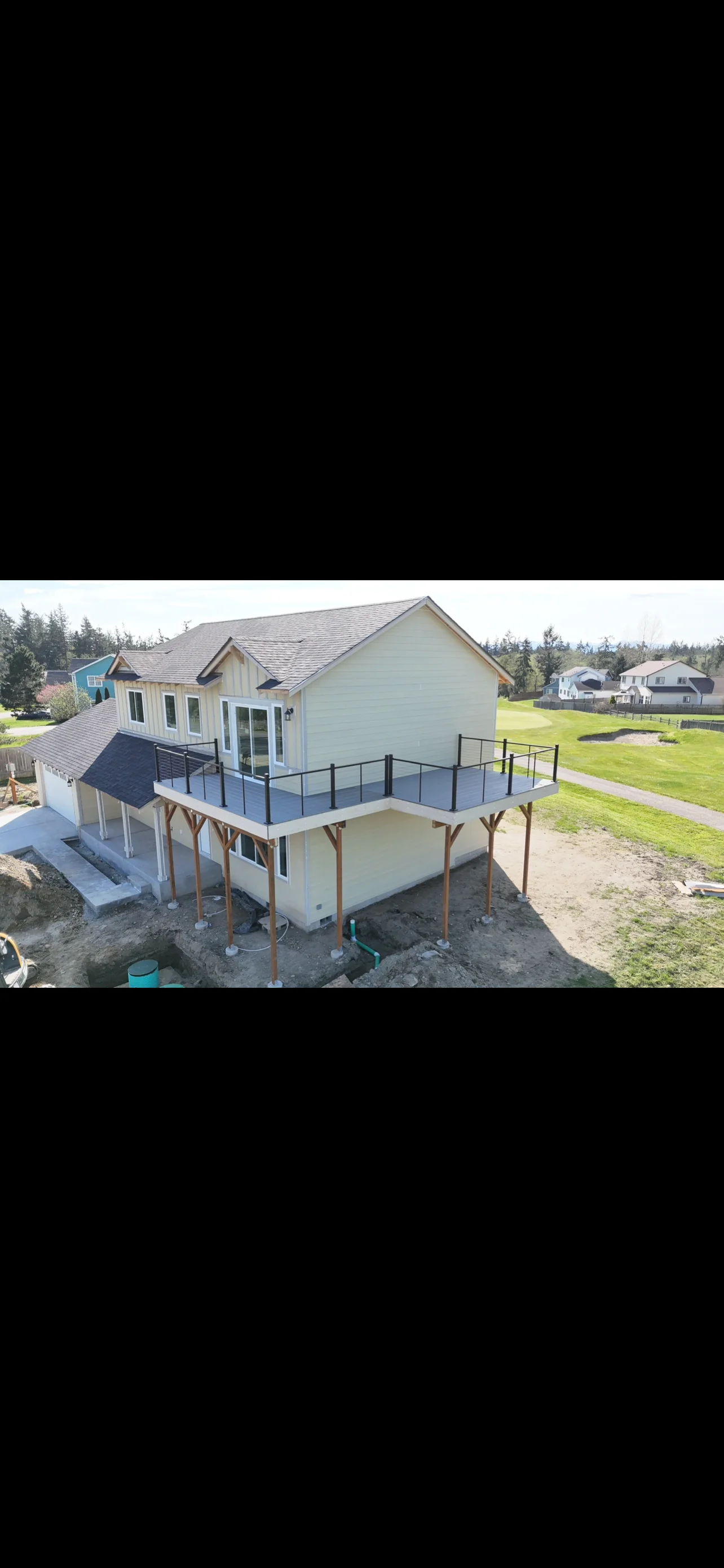 Two-story home addition with elevated deck and metal railings under construction