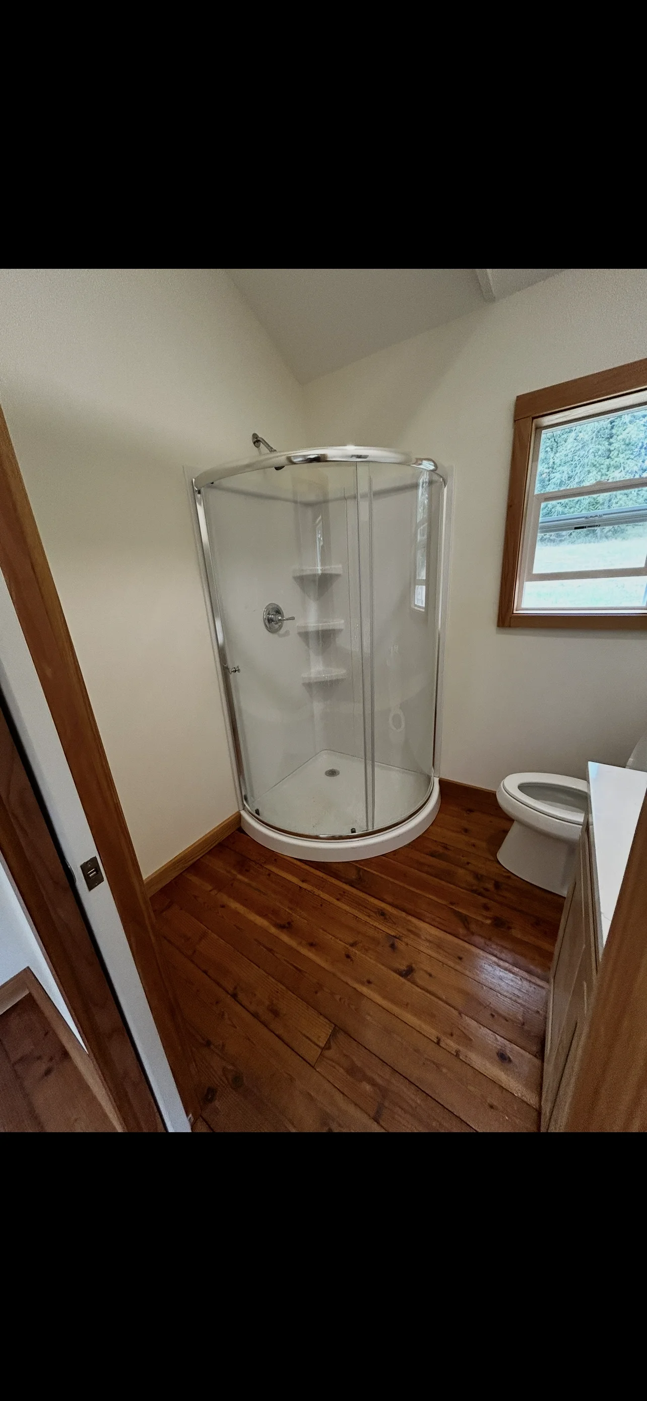 Modern bathroom with curved glass shower enclosure, hardwood floors, and white walls