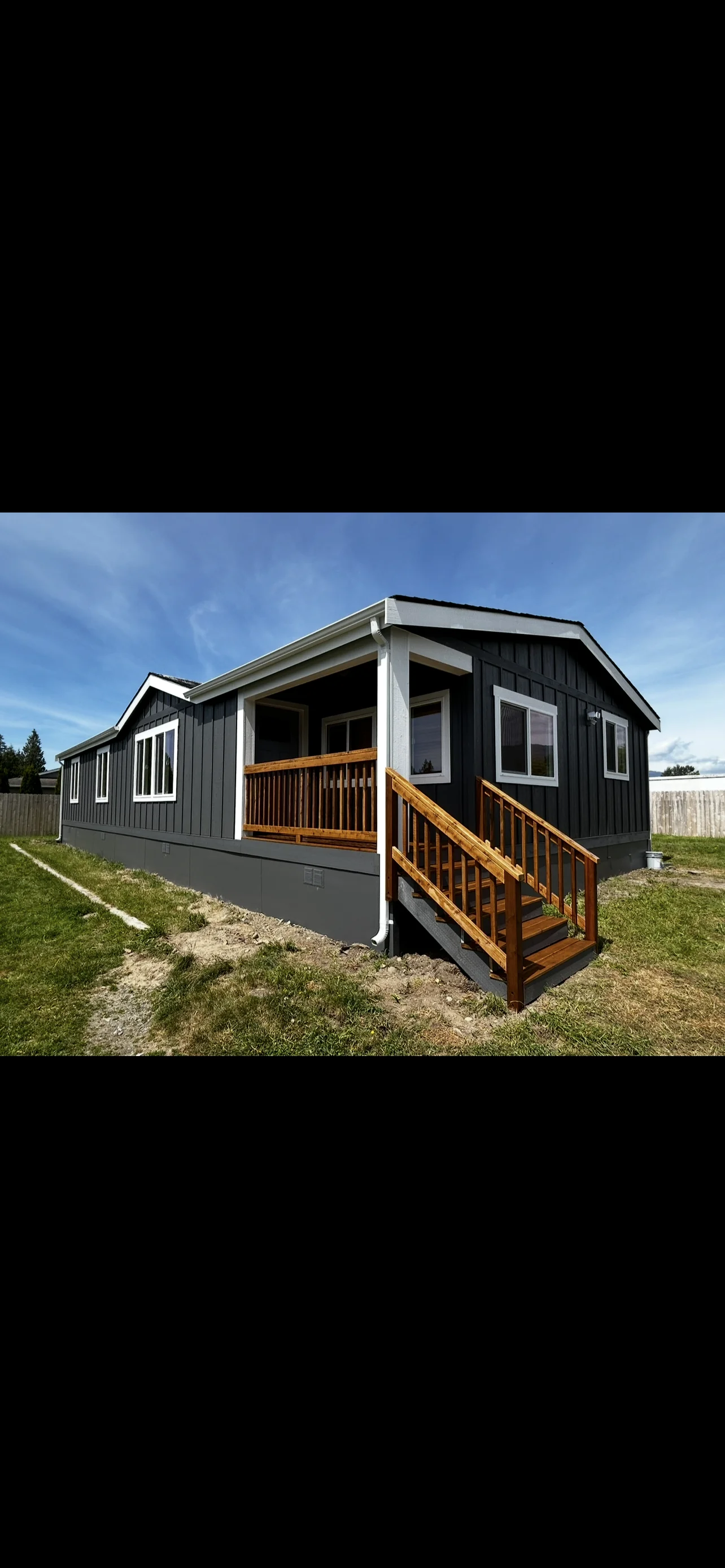 Black and white mobile home with wooden deck stairs and modern exterior finishes