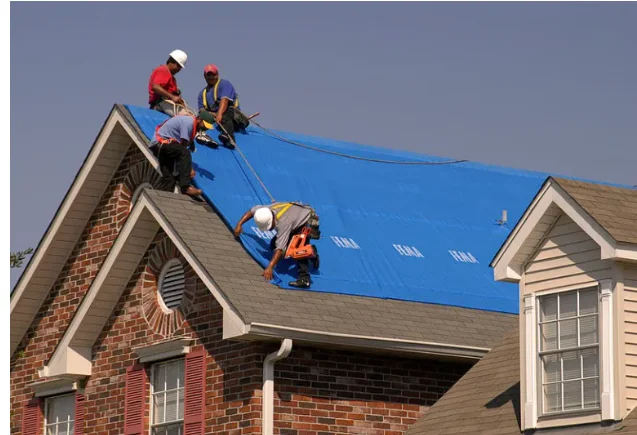 A Rio Vista Contracting roofer repairing storm-damaged shingles on a residential roof in Oak Harbor, Washington, with Whidbey Island coastal skies visible in the background. Close-up view shows replaced flashing and patched roofing sections on a steep-pitch home roof.