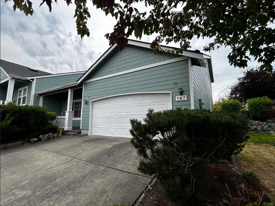 A freshly painted single-family home exterior in Oak Harbor, Washington, showing clean siding and trim with a smooth, even finish coat. The home sits in a residential Oak Harbor neighborhood with Whidbey Island's overcast coastal sky visible in the background.