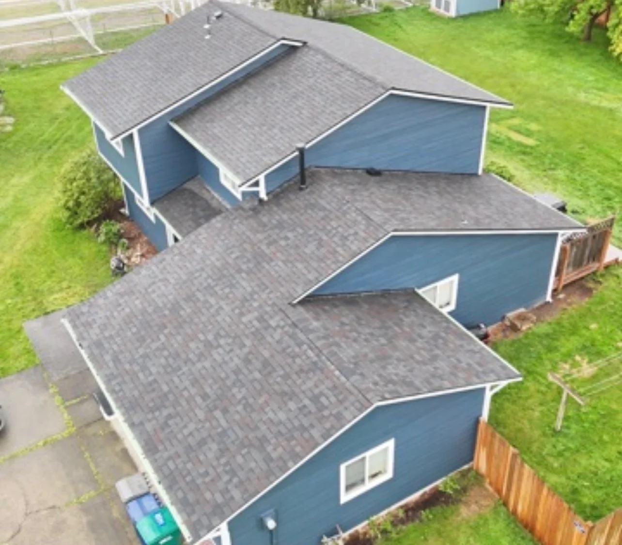 A completed roof replacement on a residential home in Oak Harbor, Washington, showing new roofing installed on a single-story house with a coastal neighborhood visible in the background. The finished roof shows clean ridge lines and uniform shingle coverage suited to the Pacific Northwest climate.
